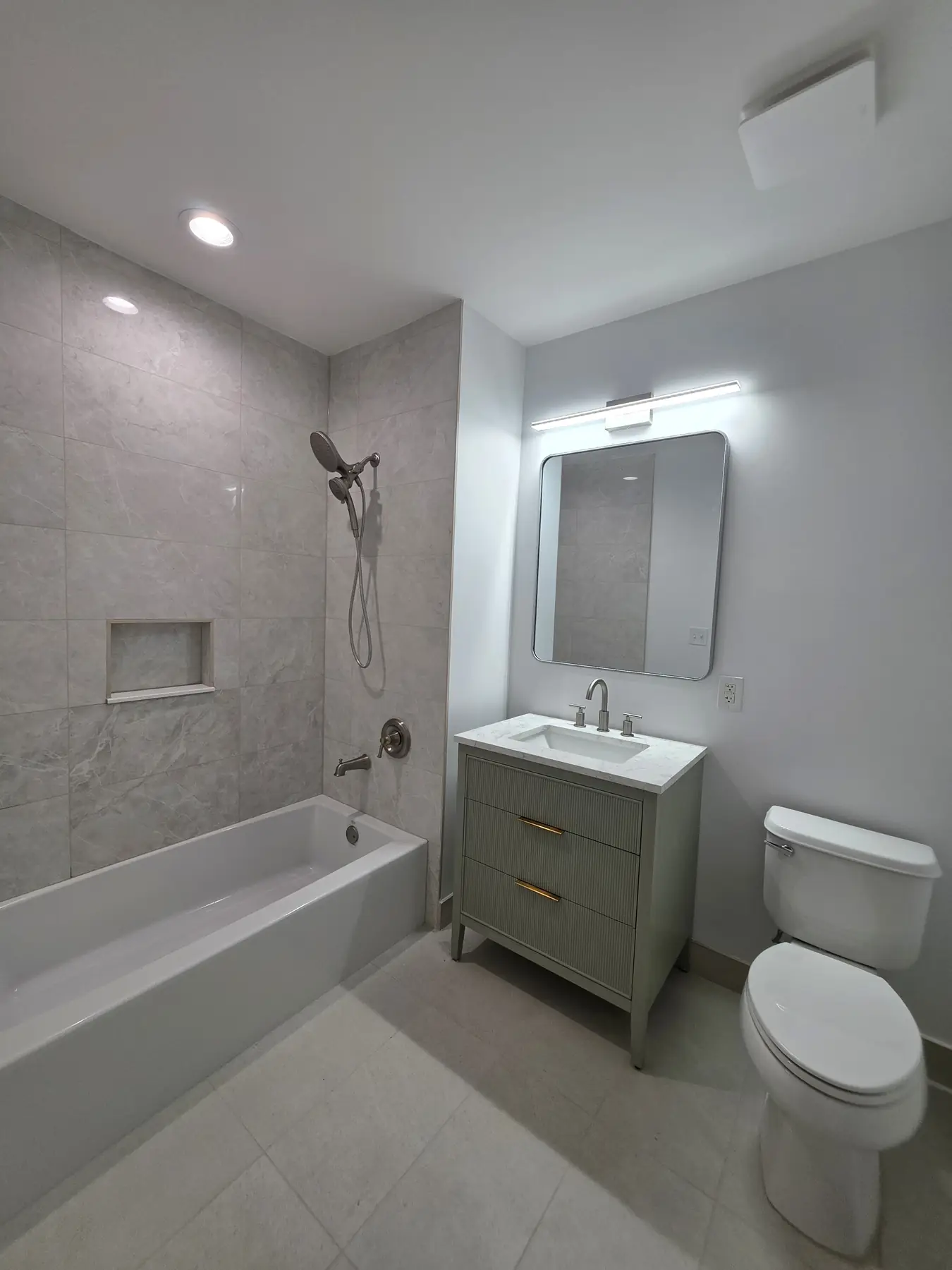The finished tub bathroom — large-format tile surround with a built-in niche