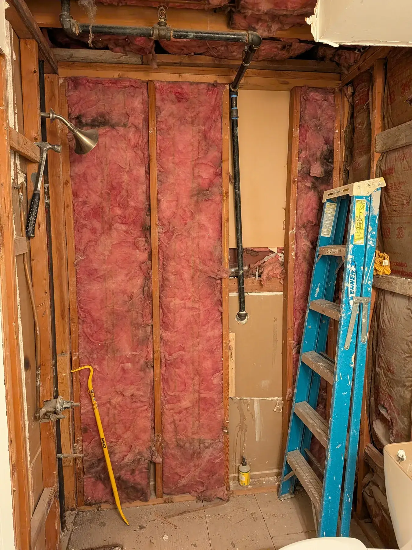 A wall opened during demolition, exposing insulation and rough plumbing