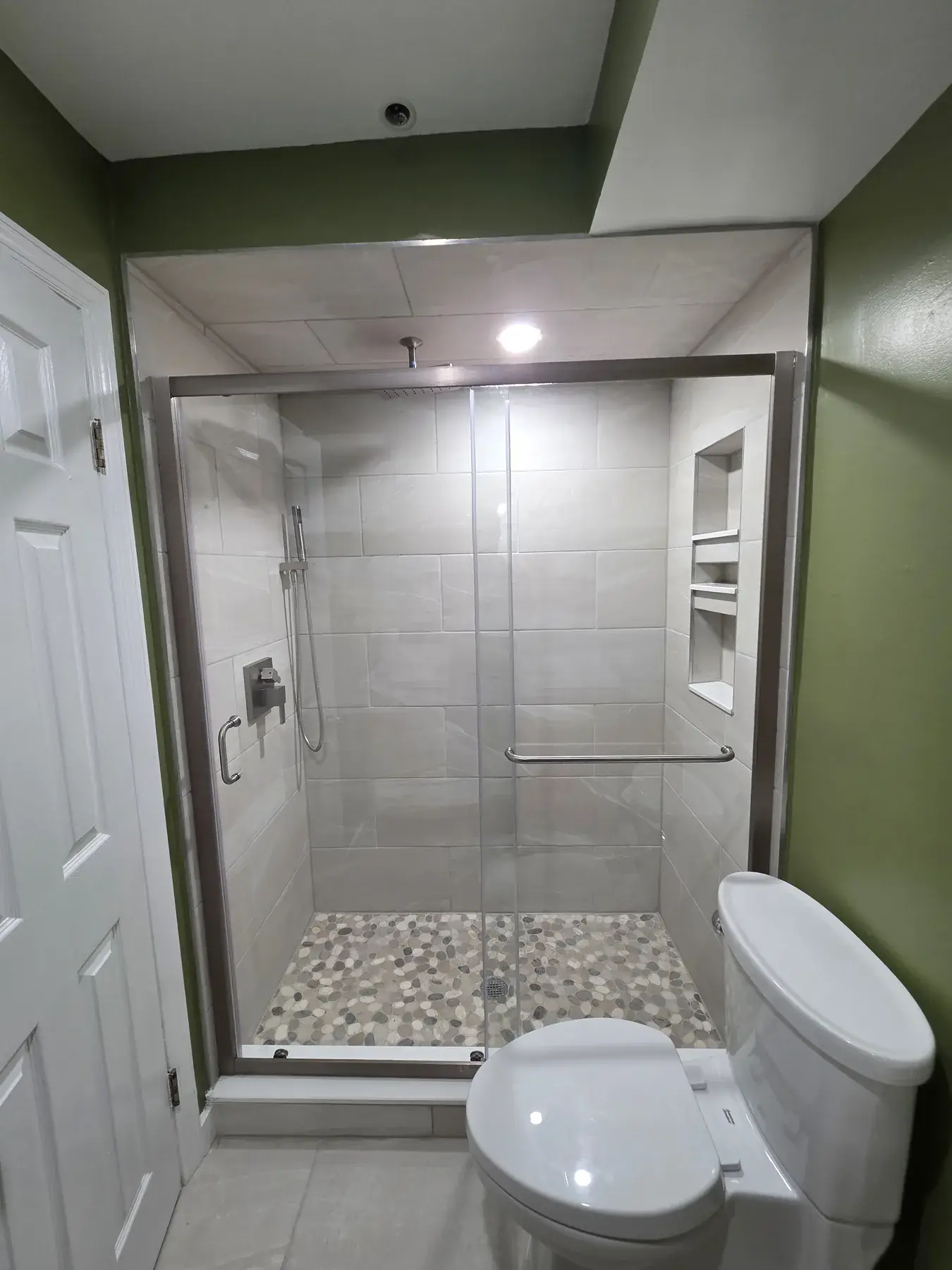 The finished walk-in shower with a glass enclosure and pebble floor, replacing the original tub