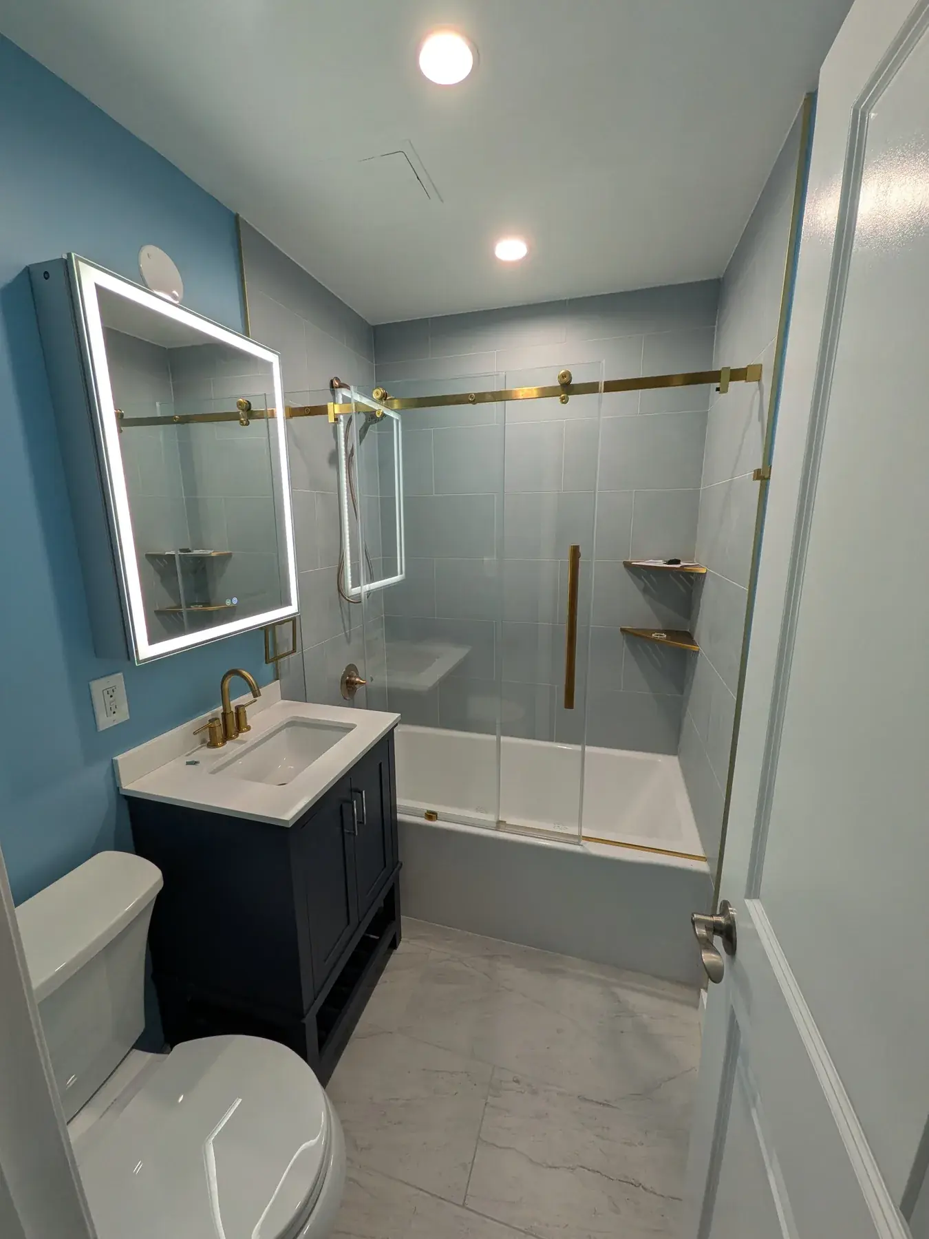 The finished bathroom with a navy vanity, backlit mirror and brushed brass fittings