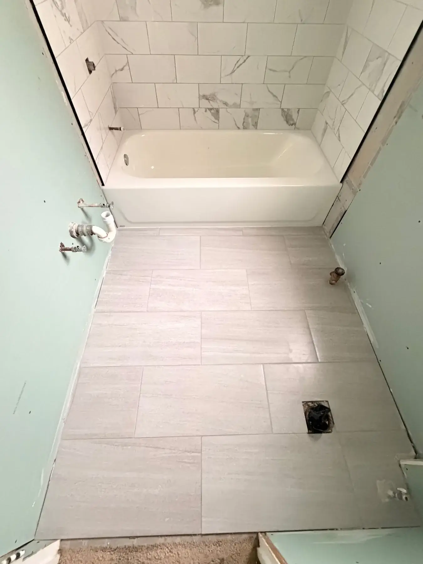 The finished bathroom with a new tub, marble-look tile surround and new floor tile